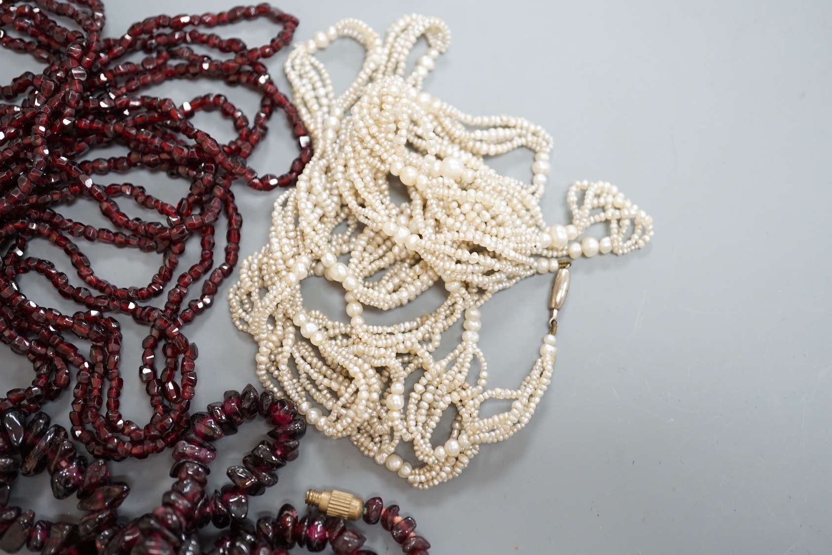 An early 20th century triple strand facet cut garnet necklace, with yellow metal clasp, 122cm, a similar single strand garnet 'pebble' necklace and a seed pearl necklace, 118cm.